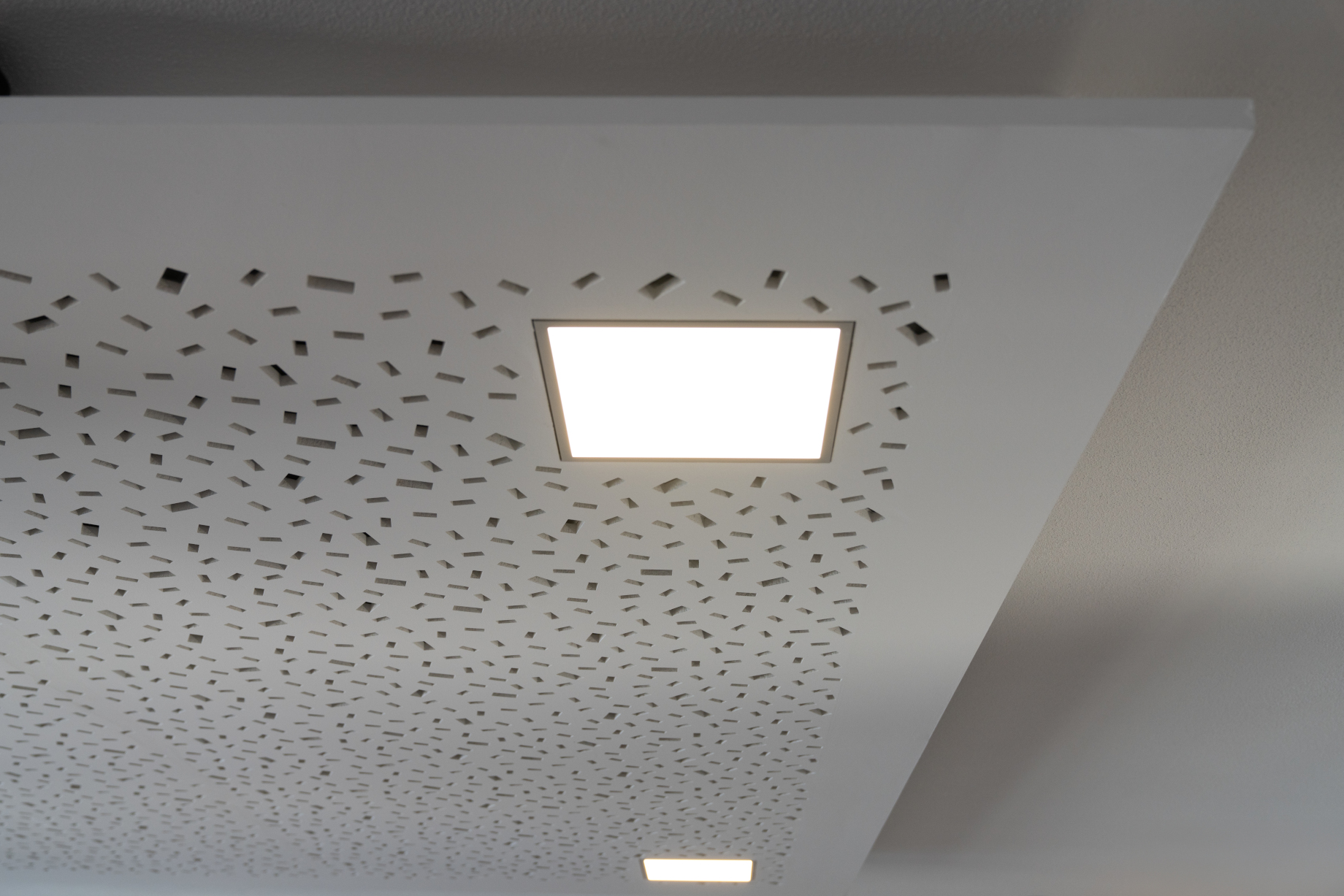 A white ceiling perforated with holes. The richter revilight is turned on, and installed in the ceiling